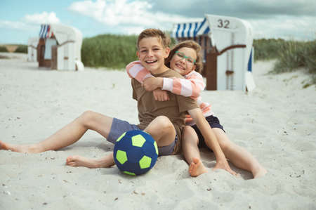 Happy teen children sitting and joyful talking on white beach at Baltic sea at summer holidaysの写真素材