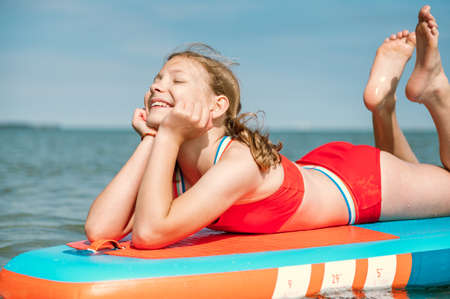 Dreaming teen girl lying on stand up paddle board and enjoy waterの写真素材