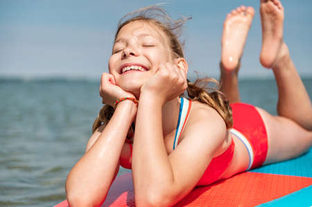Dreaming teen girl lying on stand up paddle board with closed eyes and enjoy waterの写真素材