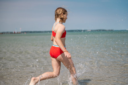 Happy teen child girl running and splashing water in turquoise sea at summer holidaysの写真素材