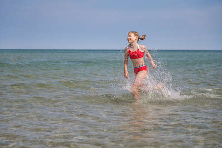 Beautiful child girl playful running in water at sea in summerの写真素材