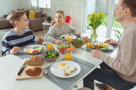 Teen children and their father talking during healthy breakfast at home in the morning before going to schoolの写真素材