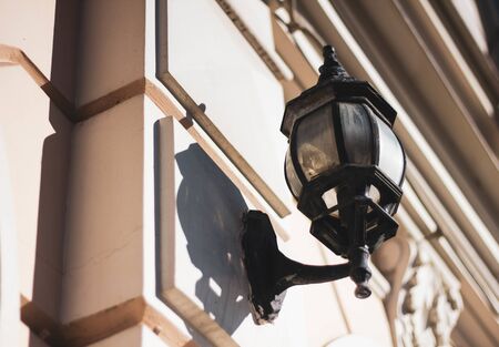 Old glass lantern in a black twisted frame on the white wall of the city building. Wall lamp on a Sunny day.の写真素材