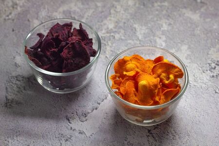 Dried carrot and beet chips in a glass bowl on a gray concrete background. Organic natural food. Top view.の写真素材