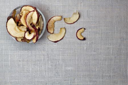 Dried Apple chips in a glass bowl on a gray textile background. Organic natural food. Top view. Flat lay. Copy space.の写真素材