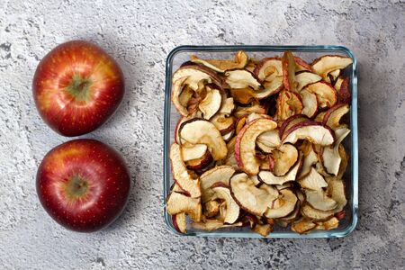 Dried Apple chips in a square glass plate and two red apples on a gray concrete background. Organic natural food. Top view. Flat lay.の写真素材