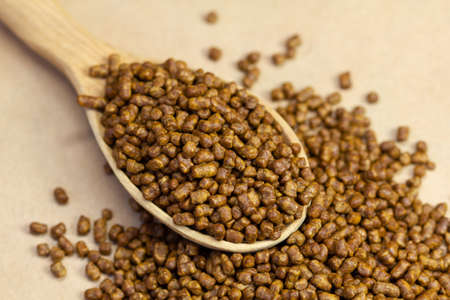 Buckwheat tea in a wooden spoon on a brown background. Buckwheat tea close-up macro photography. Scattered buckwheat tea pellets on brown background.の写真素材