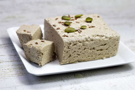 Halva close-up on a white plate on a white wooden background. Traditional oriental dessert sweet...