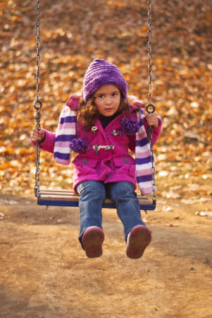little cute girl swinging at the park in autumnの写真素材