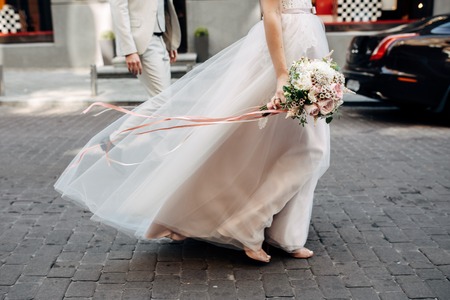 bride's hands with wedding bouquet with roses and long pink ribbonsの写真素材