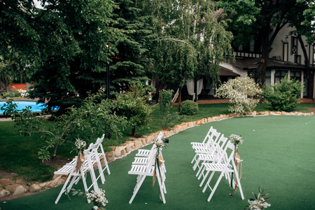 Outdoor wedding ceremony, chairs decorated with flowers and ribbons stand in rows on the grassの写真素材