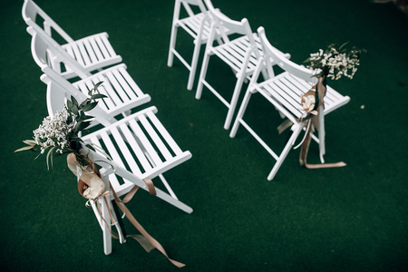 Outdoor wedding ceremony, chairs decorated with flowers and ribbons stand in rows on the grassの写真素材
