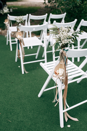 Outdoor wedding ceremony, chairs decorated with flowers and ribbons stand in rows on the grassの写真素材