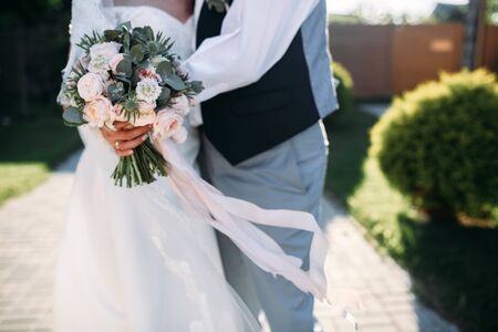 Bride's hands with wedding bouquet with eucalyptus, groom hugs herの写真素材