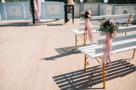 Wedding arch decorated with burgundy flowers and eucalyptus, white benches for guests decorated flowers and ribbonsの写真素材