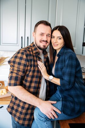 A portrait of happy couple hugging in the kitchen. Girl sitting on the table, they are laughingの写真素材