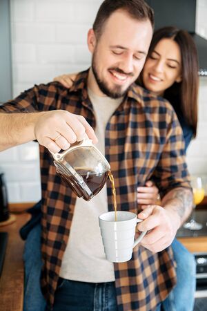 Close portrait of a young attractive couple. The guy pours coffee from the coffee pot, they are happy and laughの写真素材