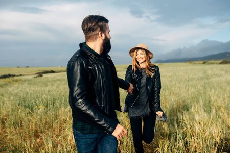 Happy loving couple walking around the field holding hands, mountains on the background