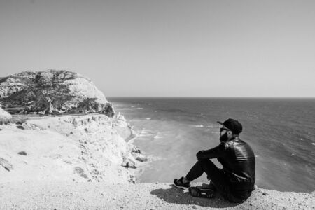 The man in a cap and the leather jacket sitting on the beachの写真素材