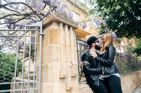 Happy couple in love hugging and laughing together, the wall is braided with purple flowers on backgroundの写真素材