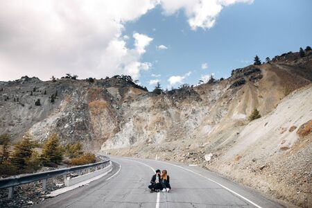 A couple in casual clothes are sitting in the middle of the road. A guy with a beard and a cap, a girl in a leather jacketの写真素材