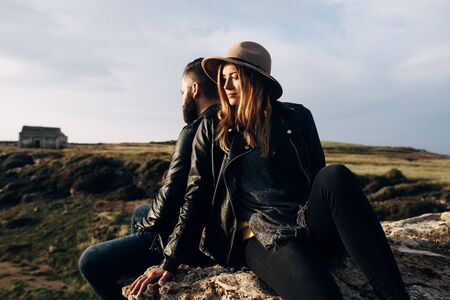 young couple sitting on a rock with a little church on backgroundの写真素材