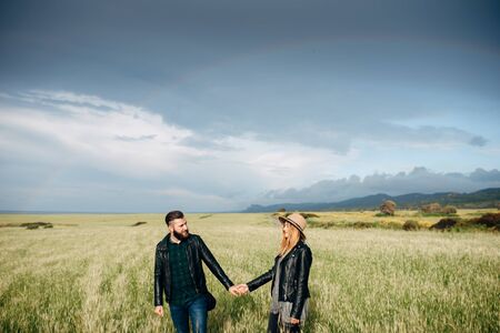 Happy loving couple walking around the field holding hands, mountains on the backgroundの写真素材