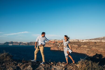 happy couple goes holding hands, the girl follows the guy with a stunning seaview on backgroundの写真素材