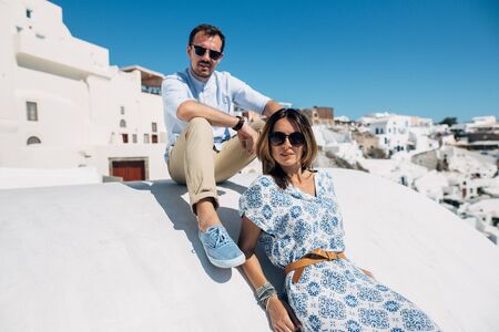 Beautiful couple in summer casual clothes and sunglasses sit on a white roof with stunning viewの写真素材