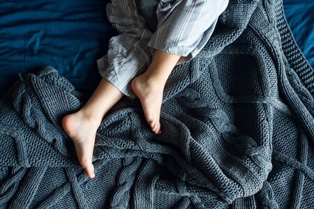 Legs of a girl in pajamas on a knitted blue plaid
