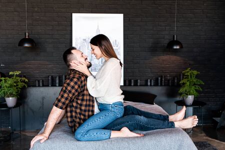 Beautiful young couple hugs sitting face to face on a large bed, side view