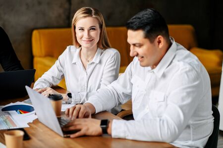 Banking workers in the office. A girl in a white shirt sits at a table facing the camera, a man in...