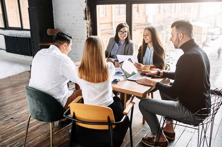 Staff meeting. Young people at the table with gadgets and laptop discuss something in a spacious modern office in the loft style.の写真素材