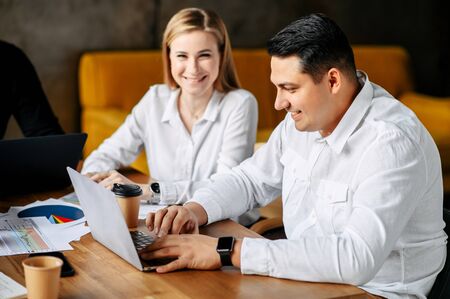 Banking workers in the office. Portrait of a man in a white shirt working with a laptop in the office, a girl in a shirt in the backgroundの写真素材