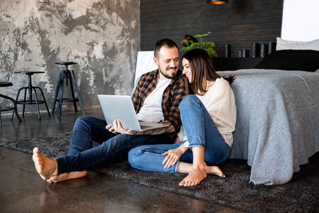Joint rest at home. Husband and wife at home watching movies and videos on a laptop in a large loft bedroomの写真素材