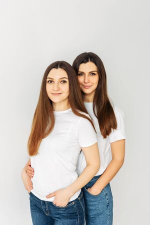 Portrait of sisters in the studio. Two similar girls in white casual t-shirts smilingの写真素材