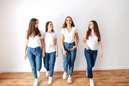 Photo in motion. Girls in white T-shirts and jeans walk and laugh. Isolated photo