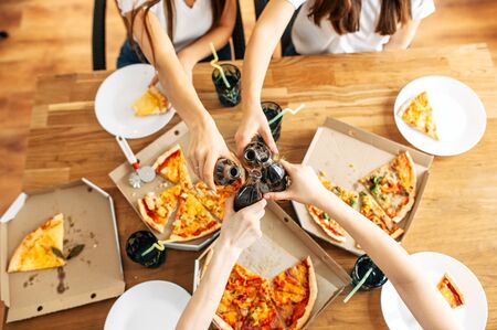 Pizza party. Cheers with bottles of cola in hands above delicious pizza. Top viewの写真素材