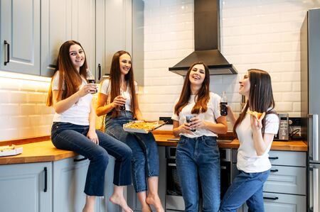 Bachelorette party with pizza at home. For attractive girls in the kitchen with slices of pizza in their hands. Some of the girls are sitting on the countertop.の写真素材