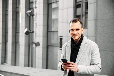 A nice positive guy in a smart casual is typing something on a smartphone. He is smiling and looking at the camera.の写真素材