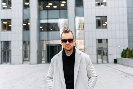 A handsome guy with a beard and in sunglasses looks at the camera in the cityscape