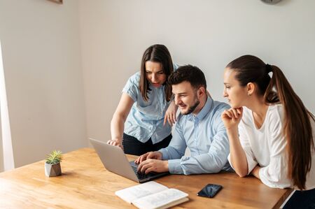 Teamwork. Young employees in a smart casual are working together on a task. They look at the laptop screen and discussの写真素材