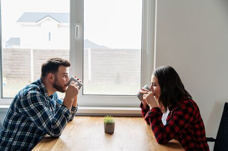 Married couple in the kitchen in a relaxed atmosphere. Young husband and wife in the kitchen drink coffee while sitting at the tableの写真素材
