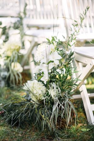 Outdoor wedding ceremony. White wooden chairs in a row on the grass, decorated with white fresh flowers and green branches.の写真素材