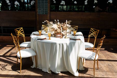 Wedding banquet on the open terrace. Boho-style festive table decorated in warm brown, gold and nude colors, a bouquet with fluffy spikelets, pampas grass and dried flowers in the middle of the tableの写真素材