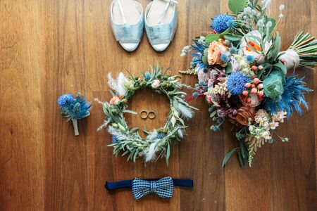 Wedding Accessories. Wedding rings in white gold, silver wedding shoes of the bride, a wreath of flowers, a bow tie and boutonniere groom in an orderly composition on the table. Close-up imageの写真素材