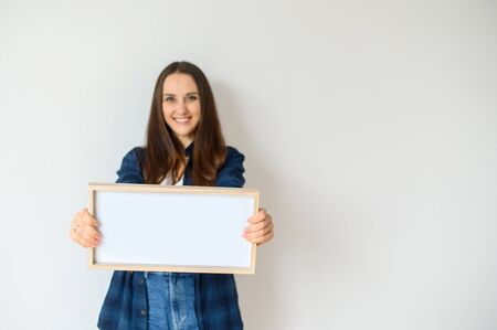 Young girl in casual clothes holding a blank sign in her hands and smiling.
