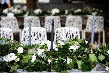 Gray candles in candlesticks among greenery and flowers on the festive table