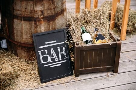 Bar at a summer party. Black plate sign bar, bottles of wine in a wooden box with a strawの写真素材
