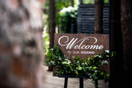 Wooden board with the inscription Welcome to our wedding decorated with green branches